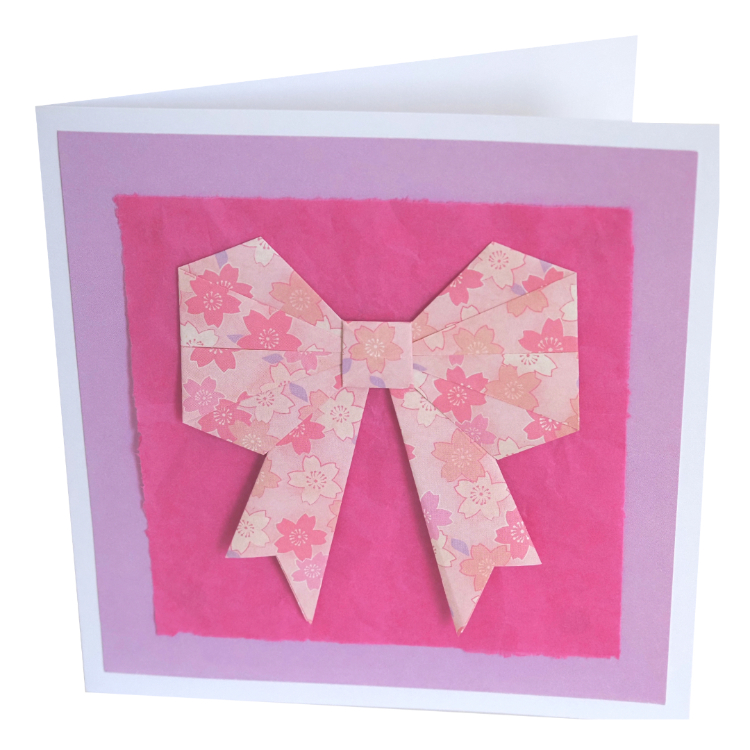 Photograph of greeting card with pink origami bow and pink tissue paper background
